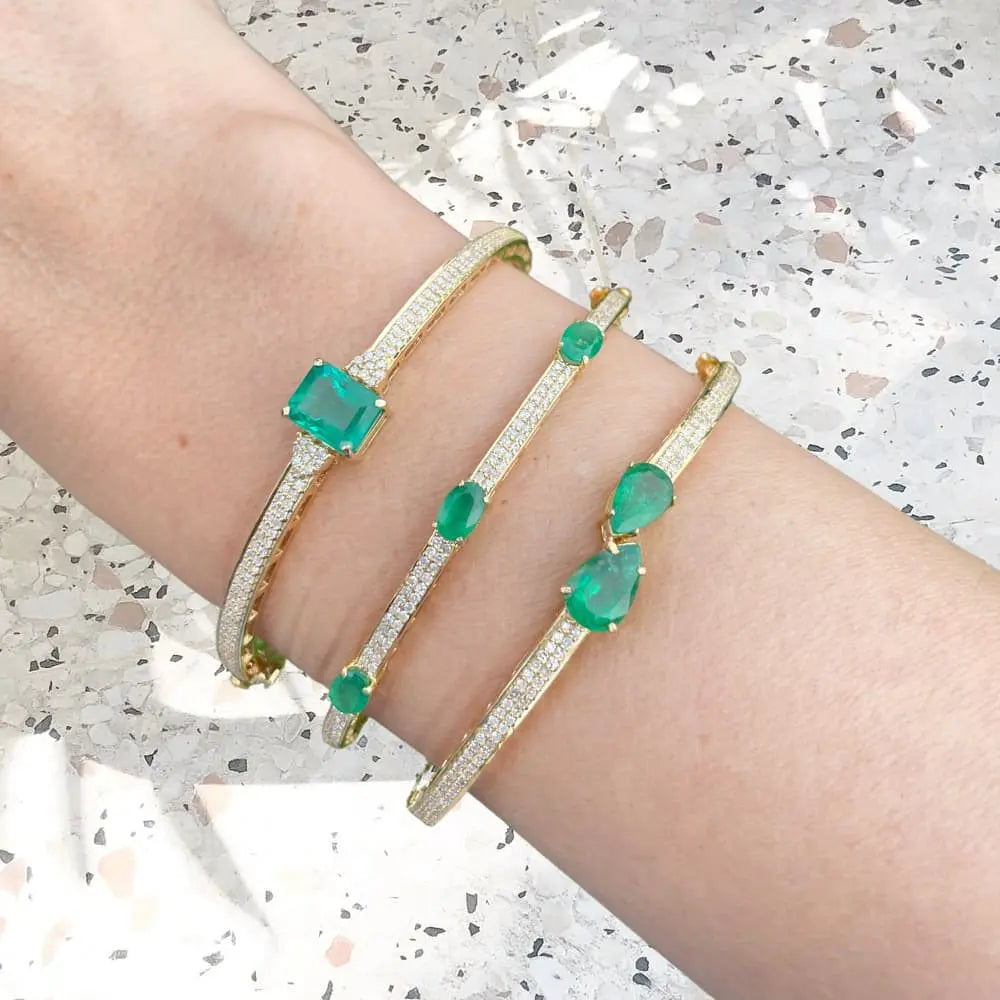 Three gold bracelets with green gemstones on a person's wrist against a speckled surface.