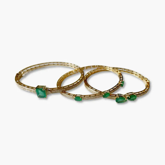 Three gold bangles with green gemstones on a white background